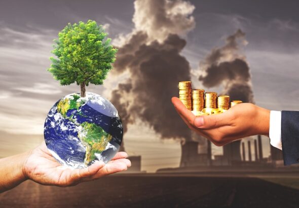 En hand hållandes jordglob, en hållandes pengar och industri i bakgrunden